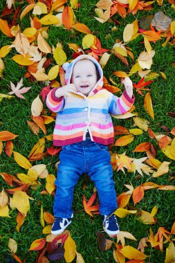 Kız çim üzerinde oturan ve renkli sonbahar yaprakları ile oynuyor
