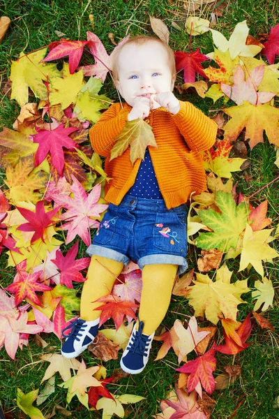 Girl sitting on the grass and playing with colorful autumn leaves — Stock Photo, Image