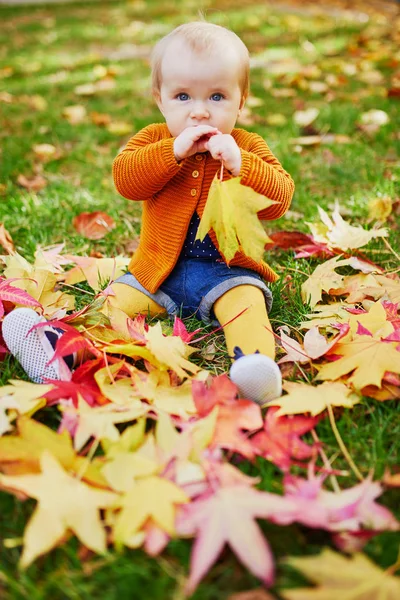 Girl sitting on the grass and playing with colorful autumn leaves — Stock Photo, Image