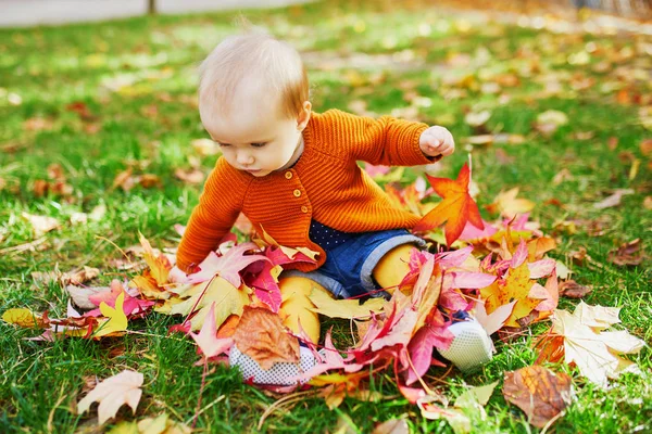Chica sentada en la hierba y jugando con hojas de otoño de colores — Foto de Stock