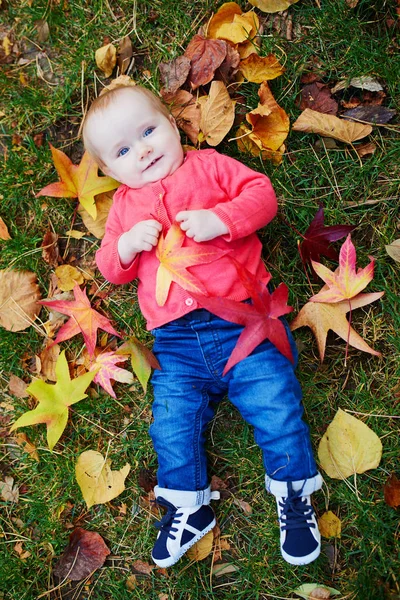 Chica sentada en la hierba y jugando con hojas de otoño de colores — Foto de Stock