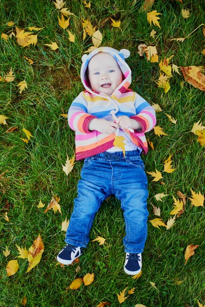 Menina sentada na grama e brincando com folhas coloridas de outono — Fotografia de Stock