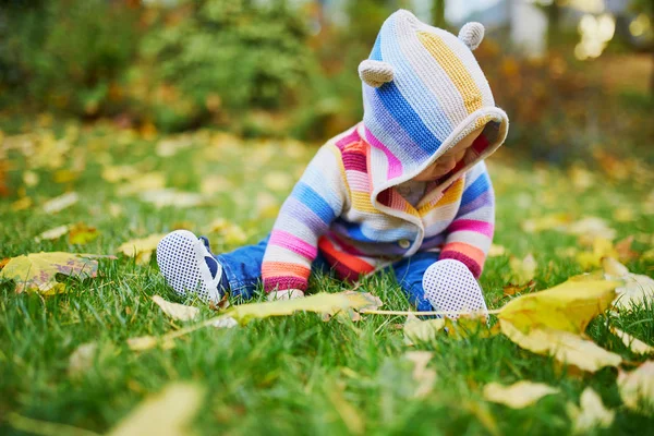 草の上に座って、カラフルな紅葉で遊ぶ女の子 — ストック写真