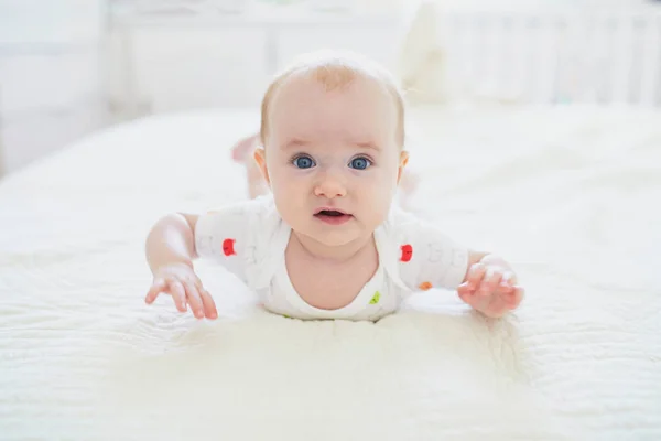 Schattig baby meisje liggend op haar buik op bed — Stockfoto