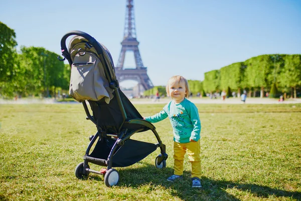 Adorable happy baby girl standing next to her pushchair in Paris near the Eiffel tower — Stock Photo, Image