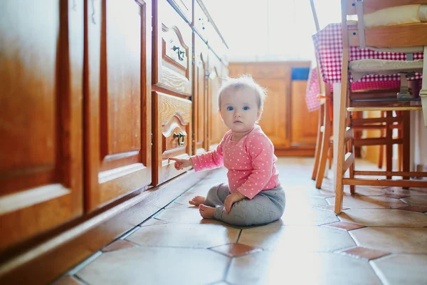 Baby flicka sitter på golvet i köket — Stockfoto