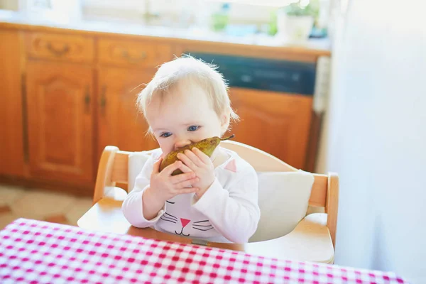 Söt liten flicka äter päron i köket — Stockfoto