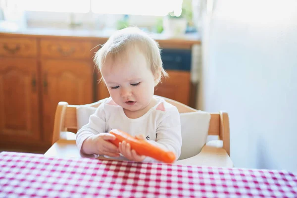 Söt liten flicka äter morot i köket — Stockfoto