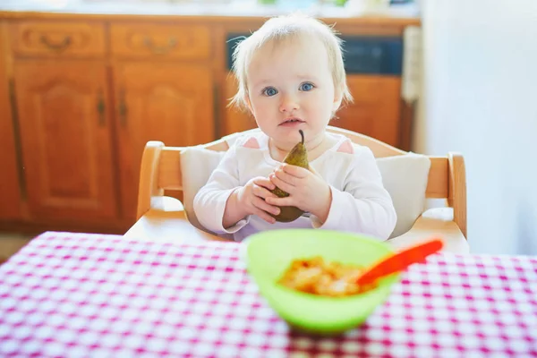 Söt liten flicka äter päron i köket — Stockfoto