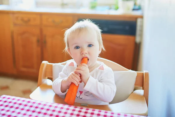 Söt liten flicka äter morot i köket — Stockfoto