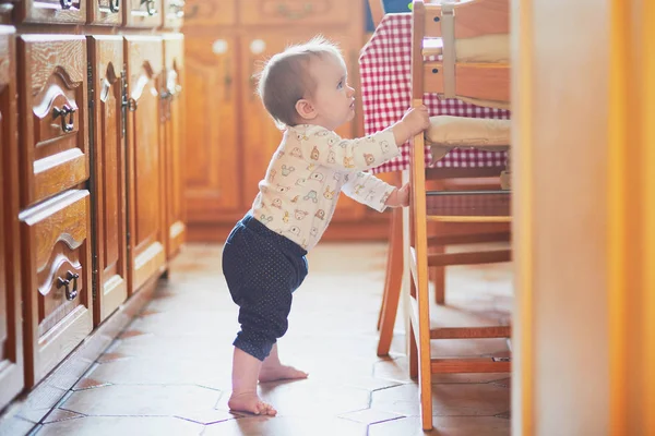 Baby meisje staande op de vloer in de keuken en vasthouden aan meubels — Stockfoto