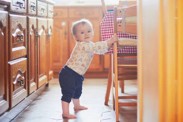 Niña de pie en el suelo en la cocina y aferrándose a los muebles —  Fotos de Stock