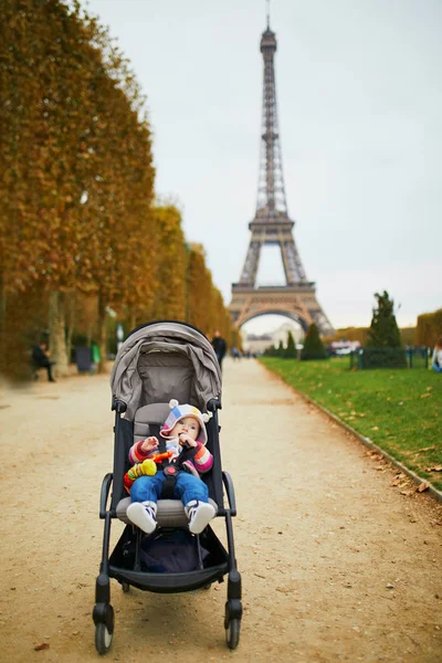 Adorable baby girl sitting in stroller near the Eiffel tower in Paris, France — Stock Photo, Image