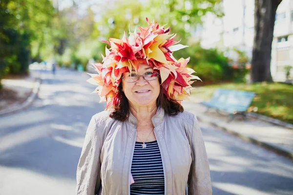 Middle aged woman in colorful maple leaves wreath walking in park on a sunny fall day — Stock Photo, Image