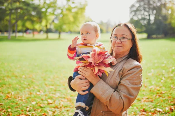 Happy middle aged woman with baby girl on sunny fall day in park — Stock Photo, Image