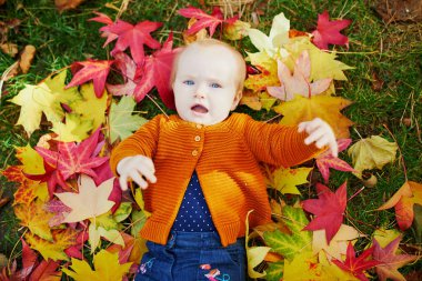 Kız çim üzerinde oturan ve renkli sonbahar yaprakları ile oynuyor