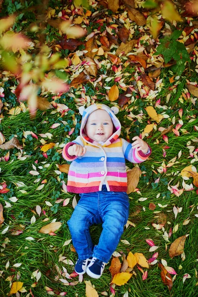 Girl sitting on the grass and playing with colorful autumn leaves — Stock Photo, Image