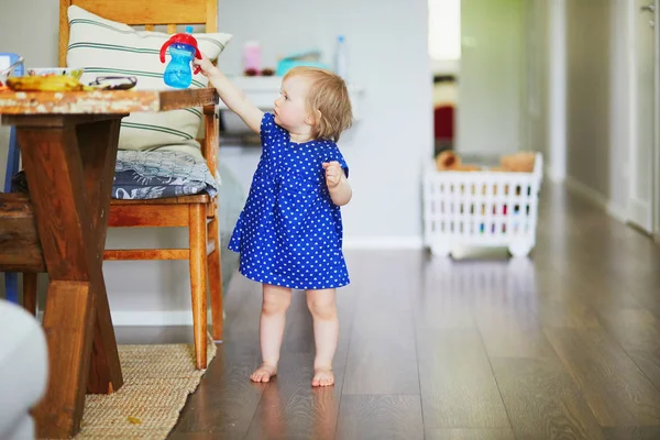 Baby flicka i blå klänning sätta henne vattenflaska på bordet — Stockfoto