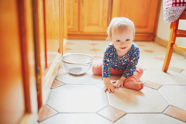 Baby flicka sitter på golvet i köket — Stockfoto
