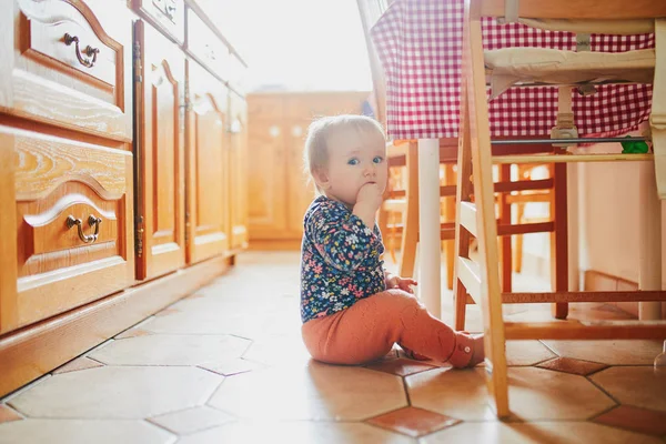 Menina sentada no chão na cozinha — Fotografia de Stock