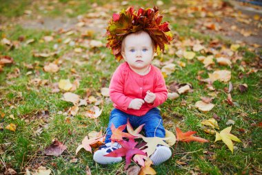 Kız çim üzerinde oturan ve renkli sonbahar yaprakları ile oynuyor