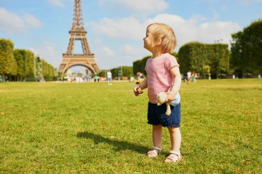 Paris, Fransa 'da Eyfel Kulesi yakınında çim üzerinde ayakta onun favori oyuncak ayı ile mutlu yürümeye başlayan kız