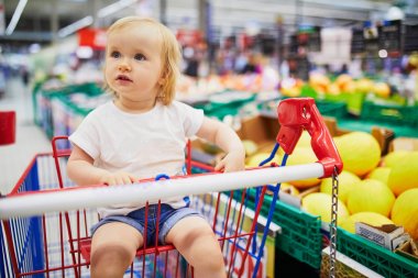 Bir gıda mağazasında alışveriş sepetinde oturan çok güzel yürümeye başlayan kız
