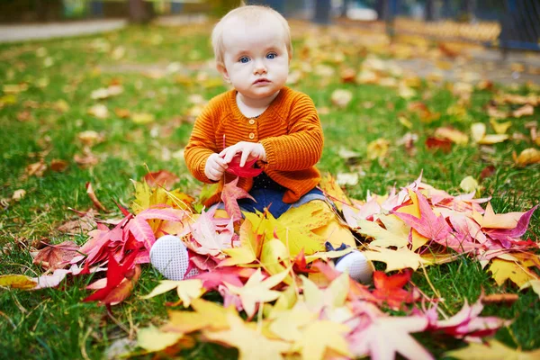 Mädchen sitzt auf dem Gras und spielt mit bunten Herbstblättern — Stockfoto
