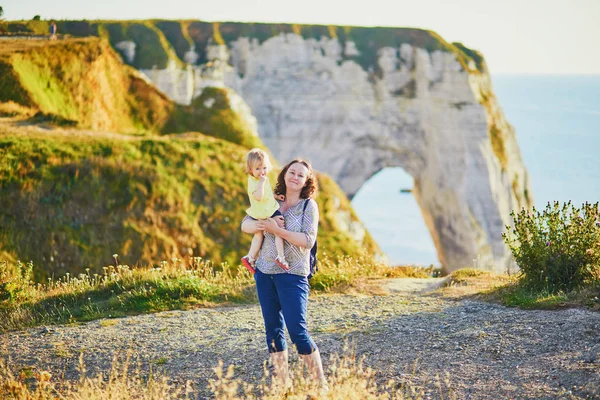 Szczęśliwy młody kobieta trzyma godny podziwu maluch dziewczyna blisko famouse Cliffs w Etretat — Zdjęcie stockowe