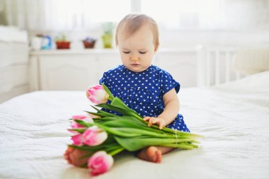 Mavi elbiseli kız pembe lalelerle oynuyor.