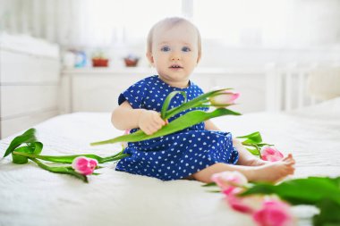 Mavi elbiseli kız pembe lalelerle oynuyor.