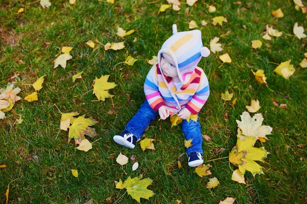 Flicka sitter på gräset och leker med färgglada höstlöv — Stockfoto