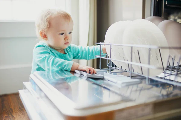 Маленький ребенок помогает разгрузить посудомоечную машину — стоковое фото