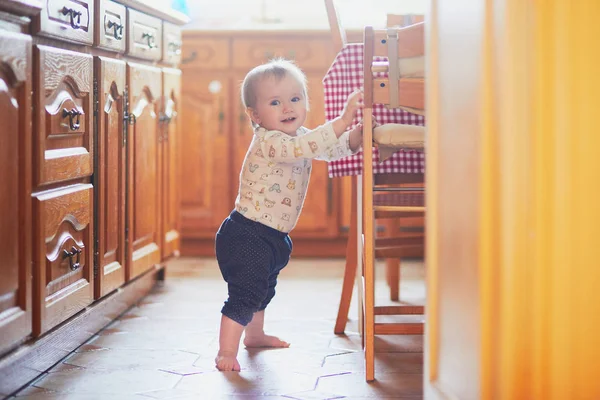 Baby Girl stående på golvet i köket och håller på att möbler — Stockfoto