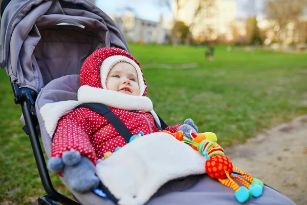 Meisje in rode jas en witte gebreide muts en sjaal zittend in kinderwagen — Stockfoto