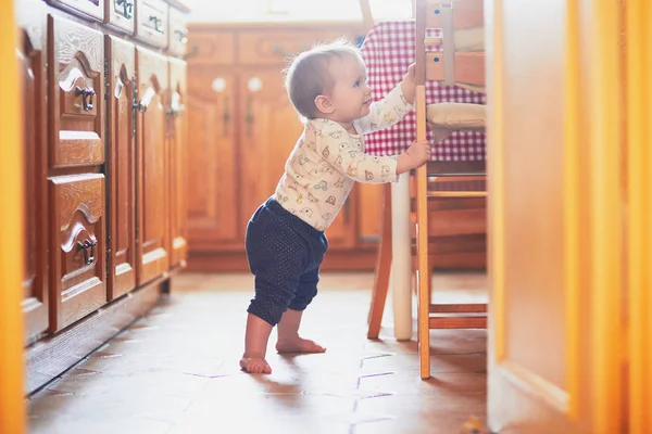 Niña de pie en el suelo en la cocina y aferrándose a los muebles —  Fotos de Stock