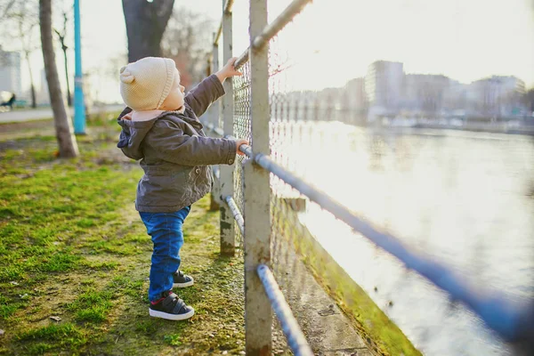 Um ano de idade menina de pé ao lado de cerca de metal no parque — Fotografia de Stock
