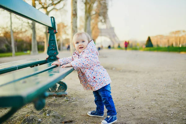 Niña de un año parada junto al banco cerca de la torre Eiffel — Foto de Stock