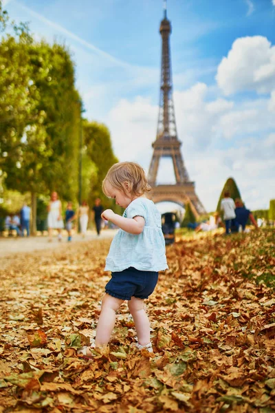 Adorable toddler girl walking on fallen autumn leaves near the Eiffel tower — Stock Photo, Image