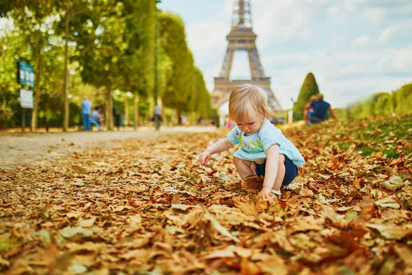 エッフェル塔の近くに落ちた秋の葉の上を歩く愛らしい幼児の女の子 — ストック写真