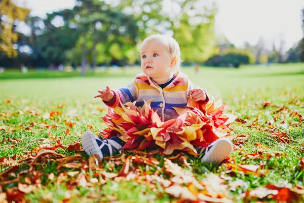 Mädchen sitzt in einem großen Haufen bunter Herbstblätter an einem Herbsttag im Park — Stockfoto