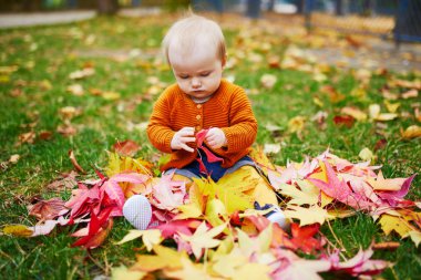 Kız çim üzerinde oturan ve renkli sonbahar yaprakları ile oynuyor