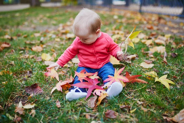 Chica sentada en la hierba y jugando con hojas de otoño de colores — Foto de Stock