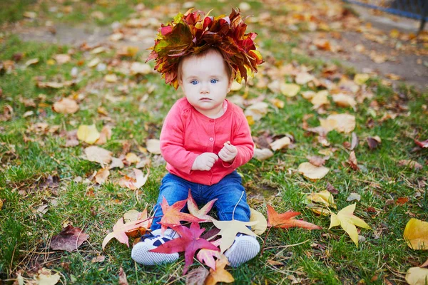 Дівчина сидить на траві і грає з барвистим осіннім листям — стокове фото