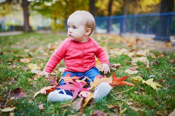 Chica sentada en la hierba y jugando con hojas de otoño de colores —  Fotos de Stock