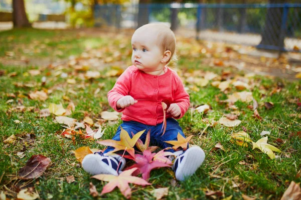 Dziewczyna siedzi na trawie i gra z kolorowych jesiennych liści — Zdjęcie stockowe