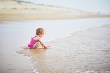Okyanus sahilinde kırmızı sulama tenekesiyle oynayan bir kız.