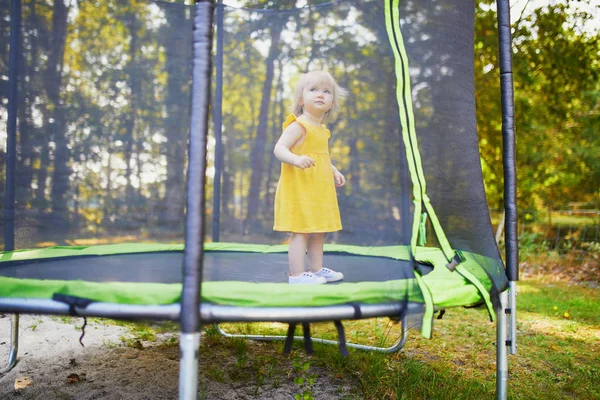 Urocza dziewczyna malucha w żółtej sukni zabawy na trampolinie w letni dzień — Zdjęcie stockowe