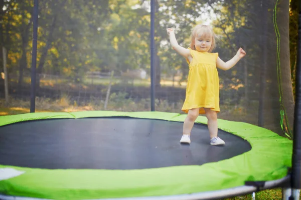 Sarı elbiseli sevimli kız yaz gününde trambolinde eğleniyor. — Stok fotoğraf