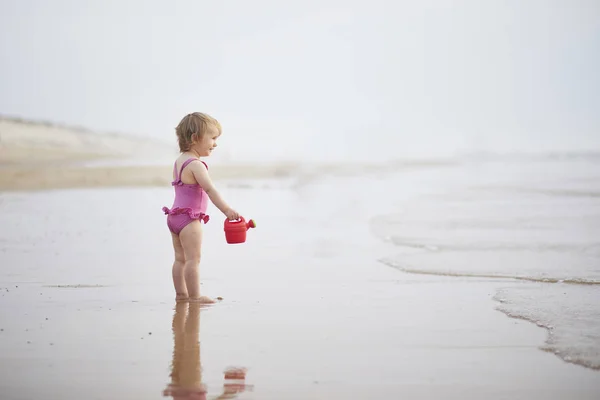 Chica jugando con rojo regadera en la playa del océano — Foto de Stock